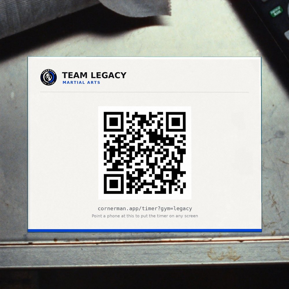 A printed card lying on a scuffed metal shelf in a gym office, carrying Team Legacy's mark and a QR code, with a television remote and a roll of hand wrap beside it